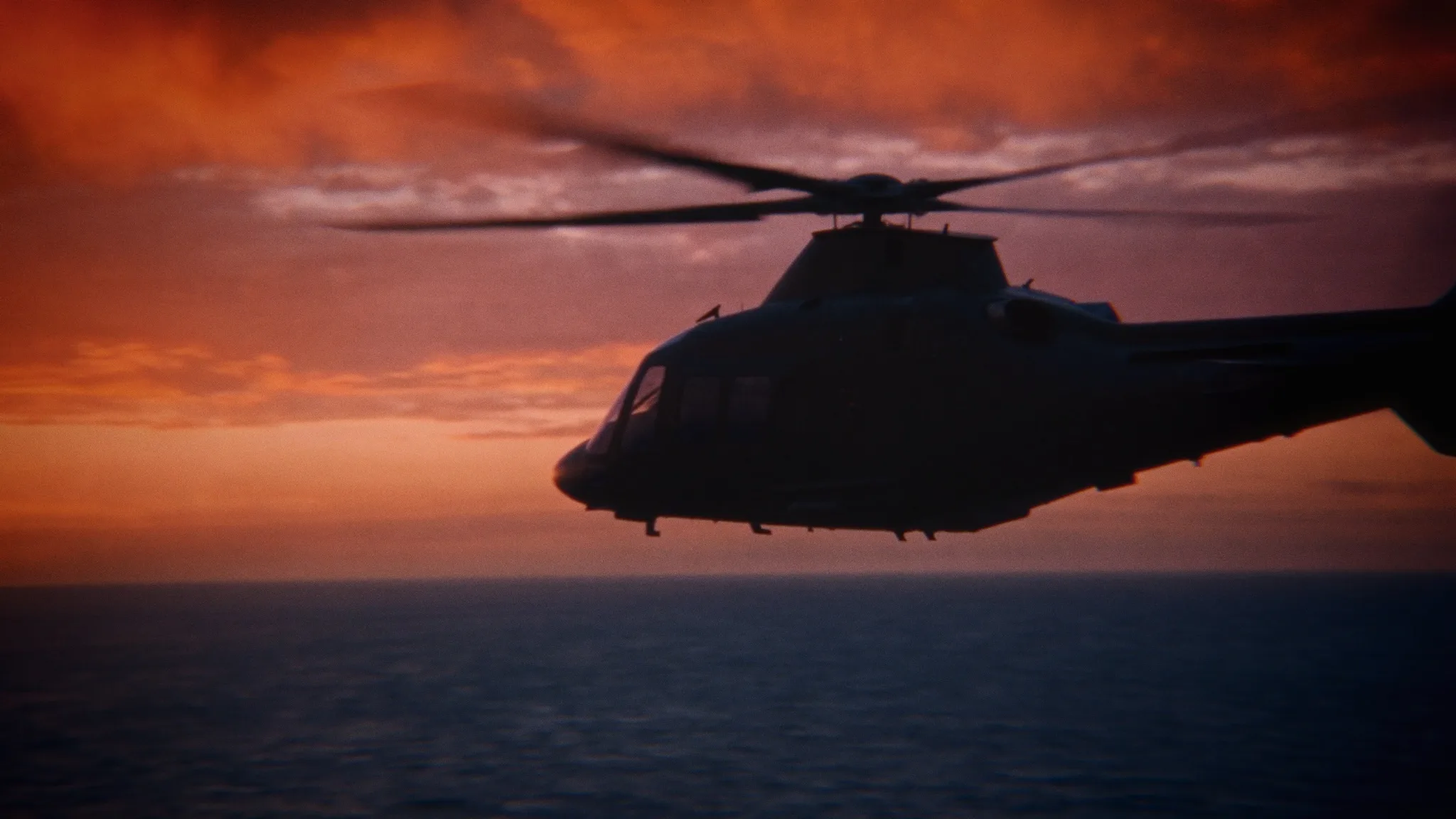 A helicopter silhouetted against a red sunset over the sea.