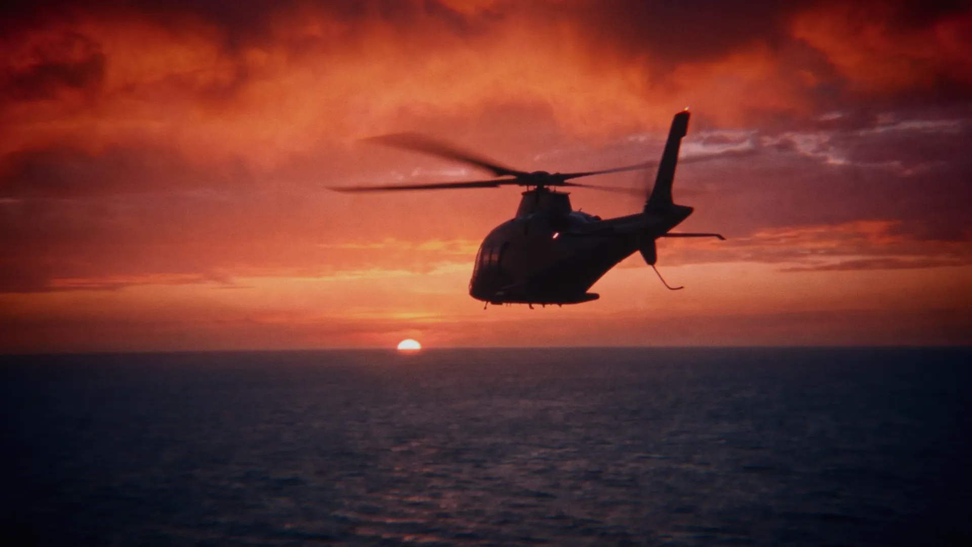 The getaway helicopter flies over the sea at sunset