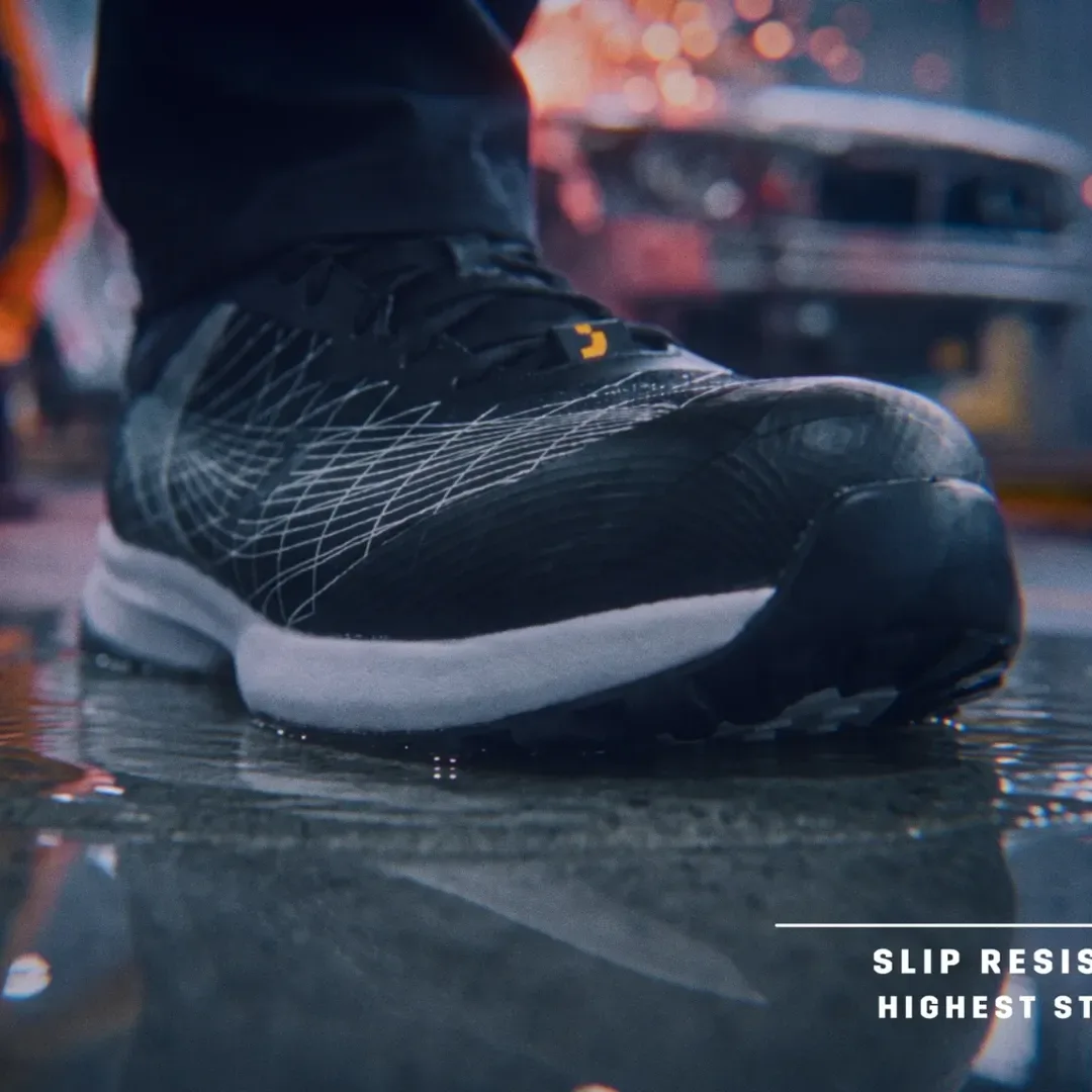 Film still, square crop: a FEATHER shoe lands on a wet car-plant floor