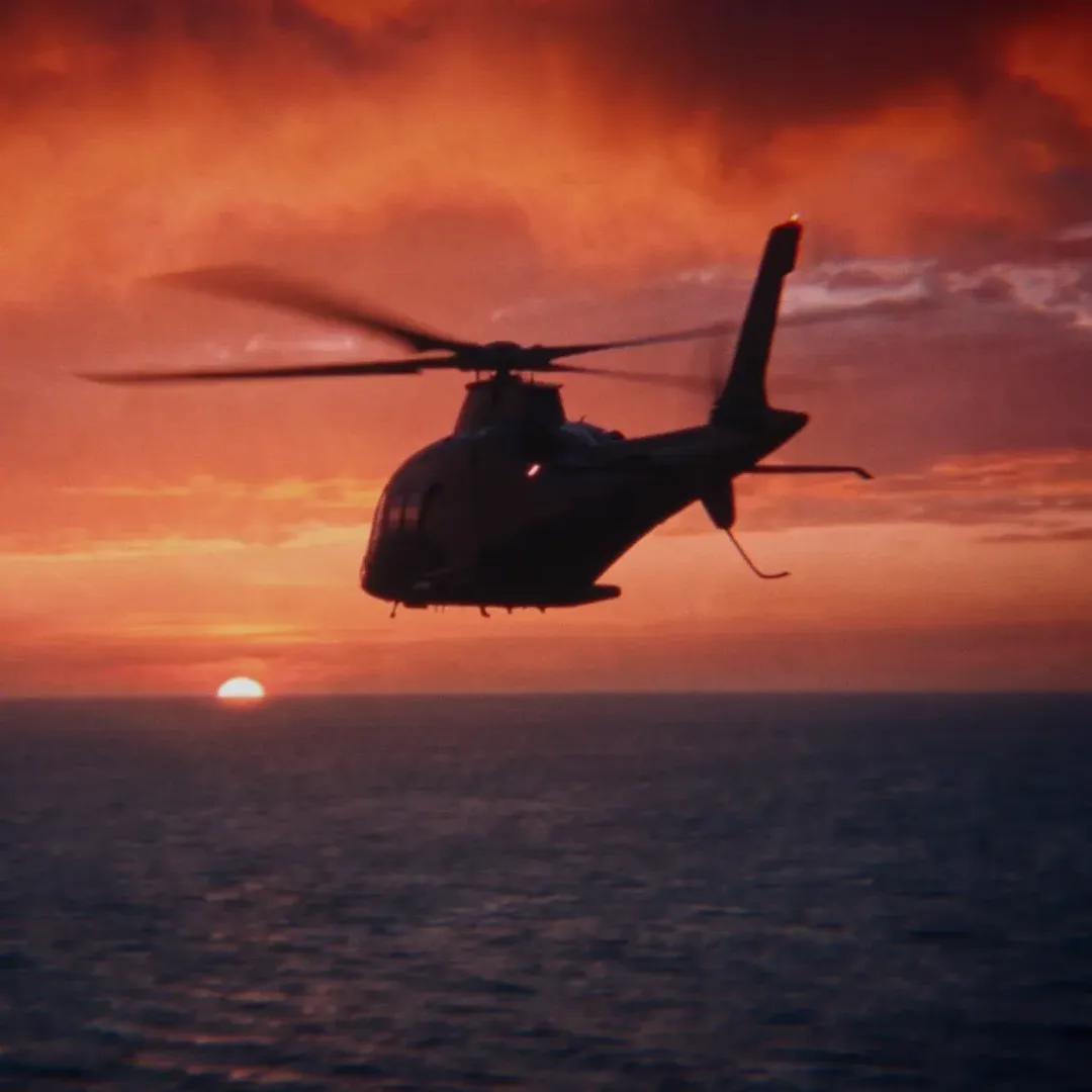 Film still, square crop: the getaway helicopter flies over the sea at sunset